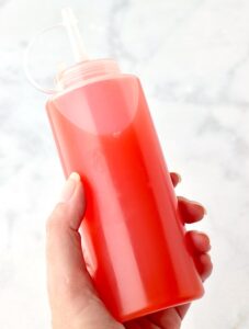 Person holding a bottle of red snow cone syrup.