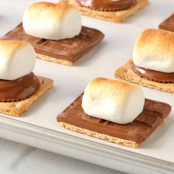 Graham crackers on lined sheet pan with chocolate and toasted marshmallows on top.
