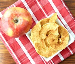 Apple chips in a white dish on a red plaid napkin.
