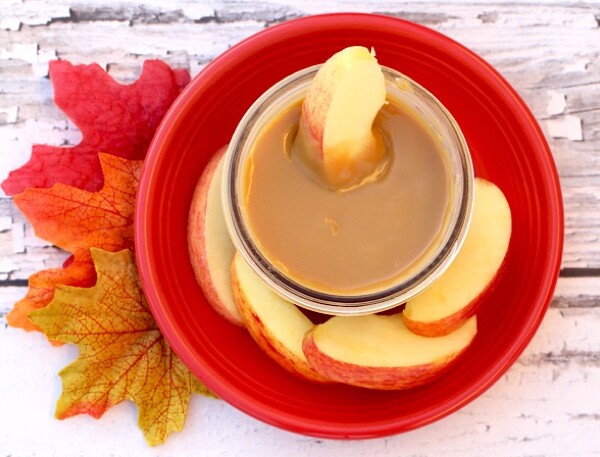 Apple slice dipping into a bowl of caramel sauce.