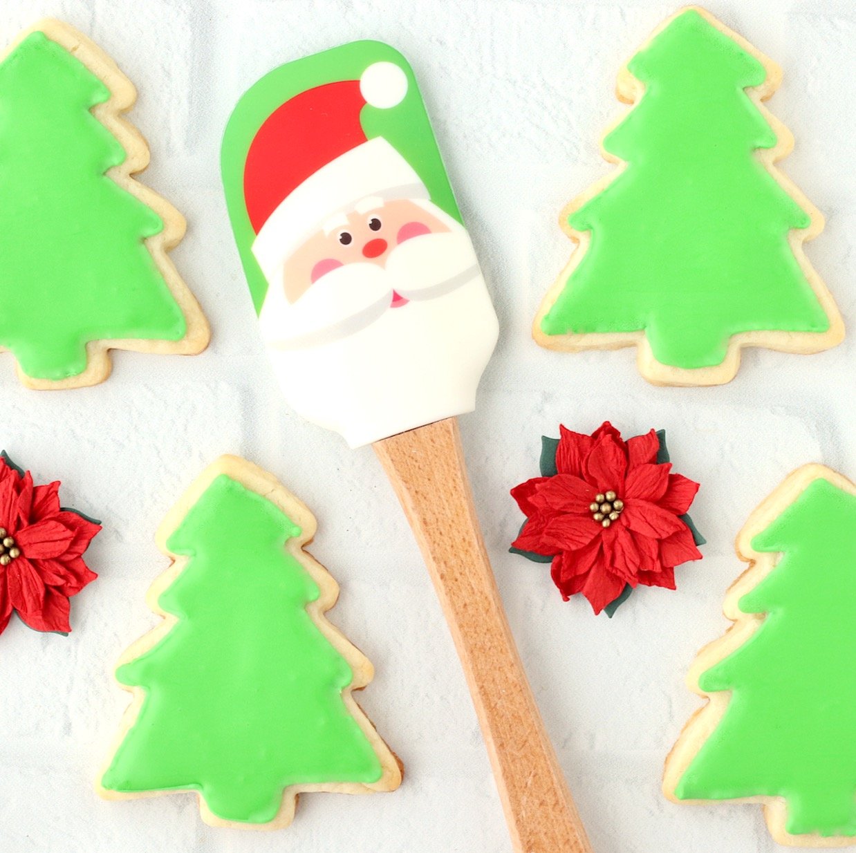 Four Christmas tree cut out sugar cookies with Santa spatula.