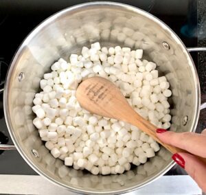 Person stirring marshmallows in a pot with a wooden spoon.