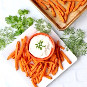Dill dip in an orange dish on plate of sweet potato fries.
