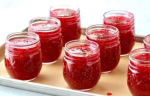 Open jars of raspberry jam on a lined baking sheet.