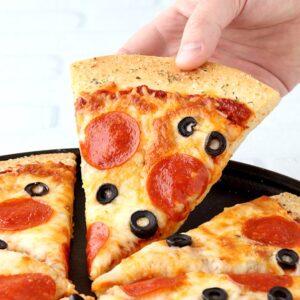 Cooked slice of pepperoni and olive pizza on baking dish being lifted up.