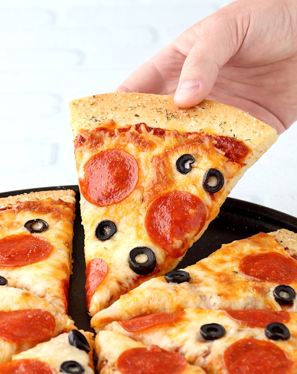Cooked slice of pepperoni and olive pizza on baking dish being lifted up.