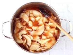Wooden spoon stirring apple pie filling in a pan.