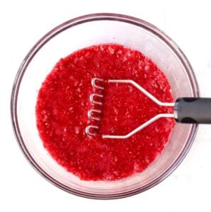 Crushed raspberries in a bowl with a masher.