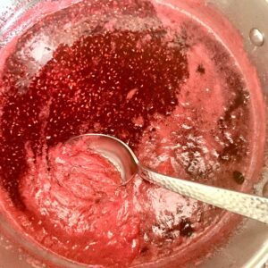Spoon skimming foam from a pot of raspberry jam.
