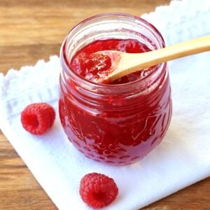 Open jar of raspberry jam with a wooden spoon.