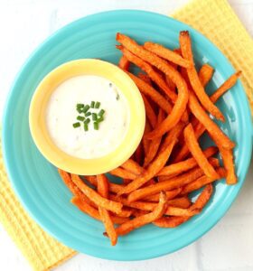 Horseradish sauce in a dish, resting on a plate loaded with sweet potato fries.