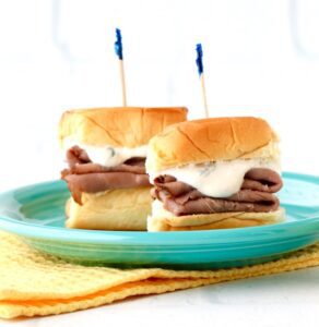 Roast beef sliders on a blue plate that is resting on a yellow napkin.