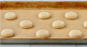 Sugared rounds of dough on a lined baking sheet.