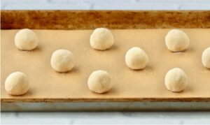 Sugared balls of dough on a lined baking sheet.