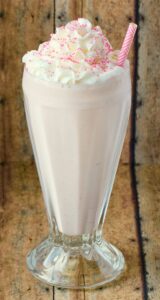 Strawberry milkshake in a tall glass topped with whipped cream.