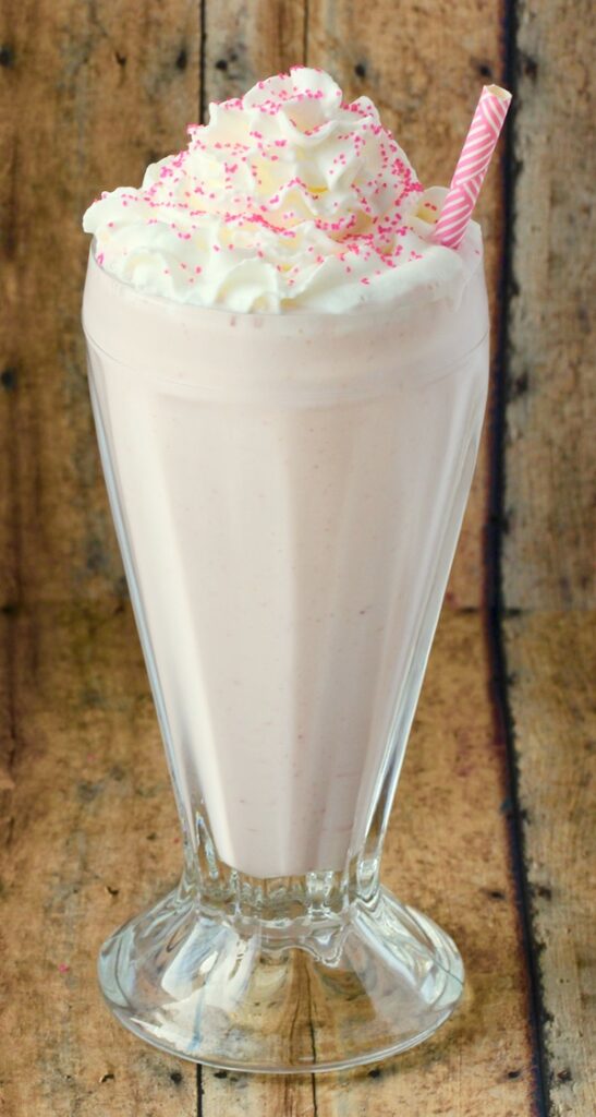 Strawberry milkshake in tall glass whip cream and sprinkles on top.