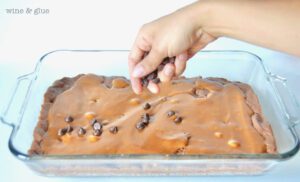 Person sprinkling chocolate chips onto caramel brownies.