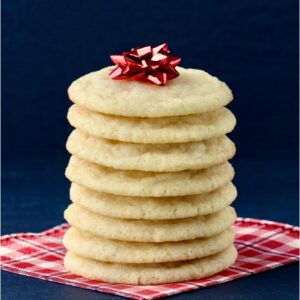 Stack of sugar cookies on napkin with red bow on top.