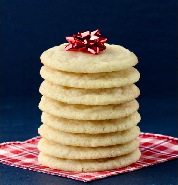 Stack of sugar cookies on napkin with red bow on top.