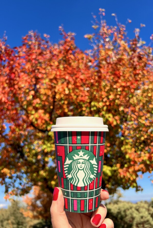 Person holding a Starbucks cup in front of a fall tree.