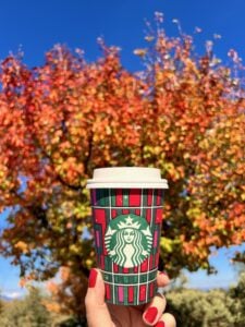 Person holding a Starbucks cup in front of a fall tree.