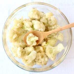 Spoon scooping cauliflower from a glass bowl.
