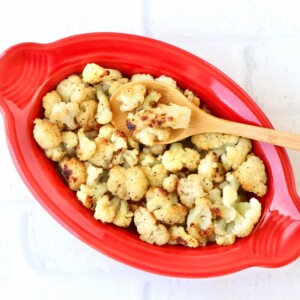 Wooden spoon scooping Roasted Cauliflower from a red bowl.