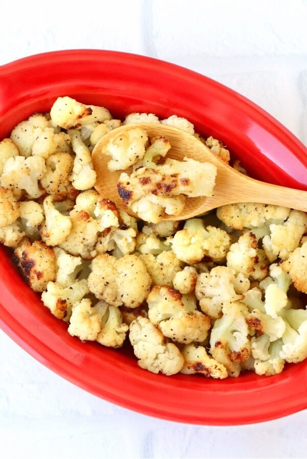 Wooden spoon scooping Roasted Cauliflower from a red bowl.