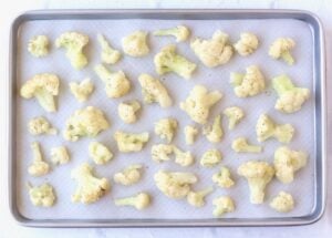 Seasoned cauliflower florets on a lined baking sheet.