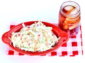 Coleslaw in a red, oblong bowl on a red and white checkered tablecloth.