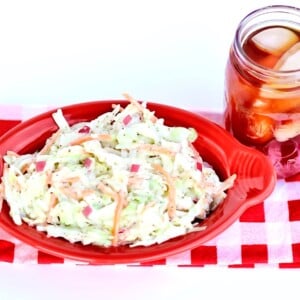 Coleslaw in a red, oblong bowl on a red and white checkered tablecloth.