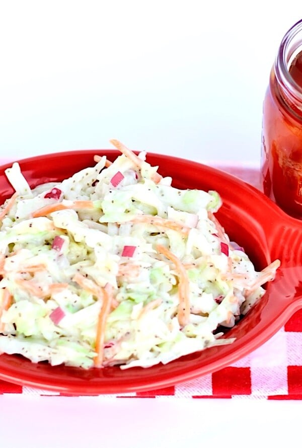 Coleslaw in a red, oblong bowl on a red and white checkered tablecloth.