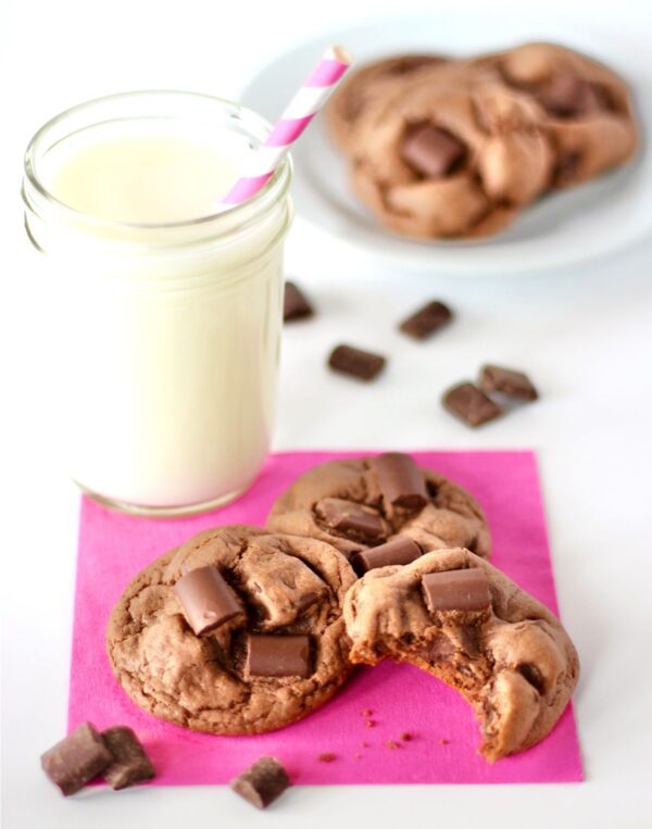 Chocolate Chunk Cookies on pink napkin with a glass of milk and chocolate chunks behind.