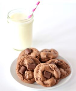 Chocolate Chunk Cookies on a white plate with a glass of milk behind.