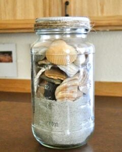 Sand and seashells stacked in mason jar.