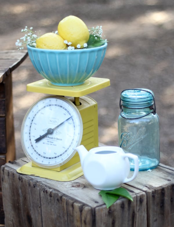 Lemons on vintage scale with mason jar and teapot to the side.