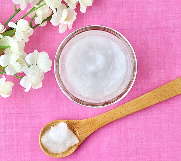 Spoon with a scoop of coconut oil hair mask next to a jar.