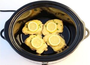 Cooked pork chops in slow cooker with lemon garlic sauce and lemon slices.
