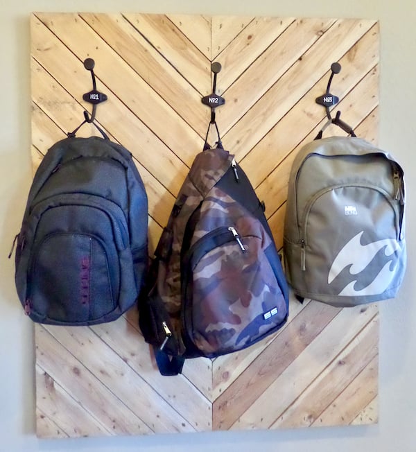 Three backpacks hanging on hooks on wall.