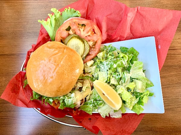 A burger and caesar salad in a basket with red paper.