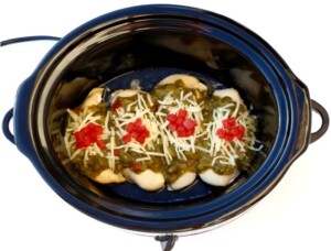 Cooked chicken in slow cooker with salsa verde and shredded cheese on top.
