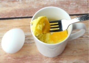Scrambled eggs in mug with bite on fork.