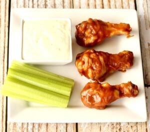 Three chicken wings on plate with celery sticks and ranch dipping sauce.