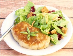 Cooked pork chop with sauce and a side salad on plate.