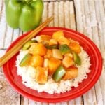 Sweet and sour chicken with bell pepper and pineapple over rice on plate with chopsticks.