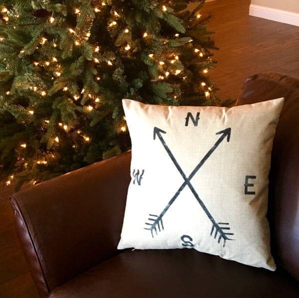 Throw pillow on corner of couch with Christmas tree in the background.