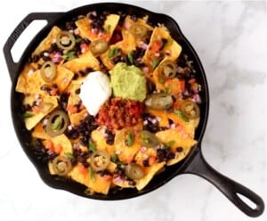 Vegetarian nachos in skillet with sour cream, guacamole, and salsa on top.