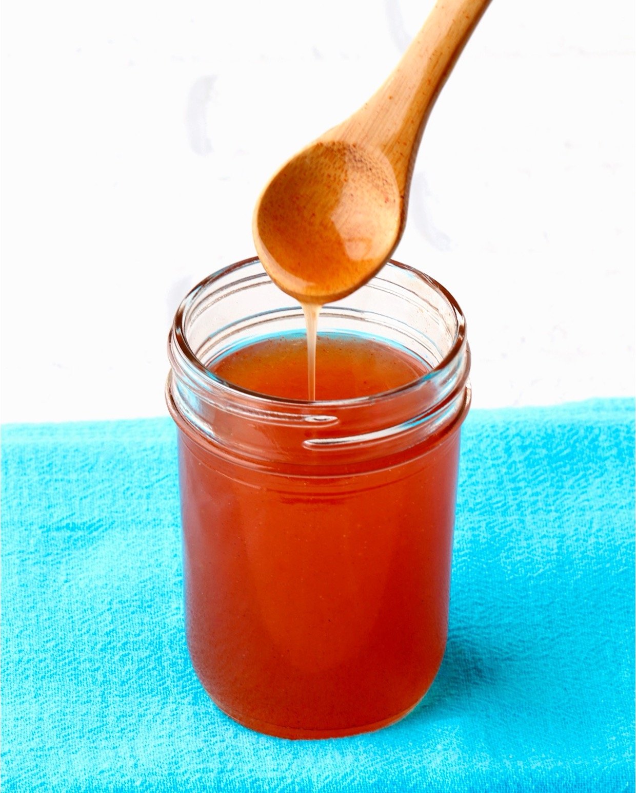 Sweet and sour sauce dripping off spoon into mason jar.