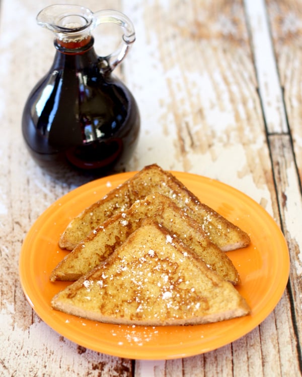 French Toast slices on an orange plate with a jar of syrup in the background.