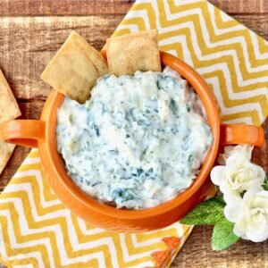 Artichoke dip in bowl with chips dipped in.